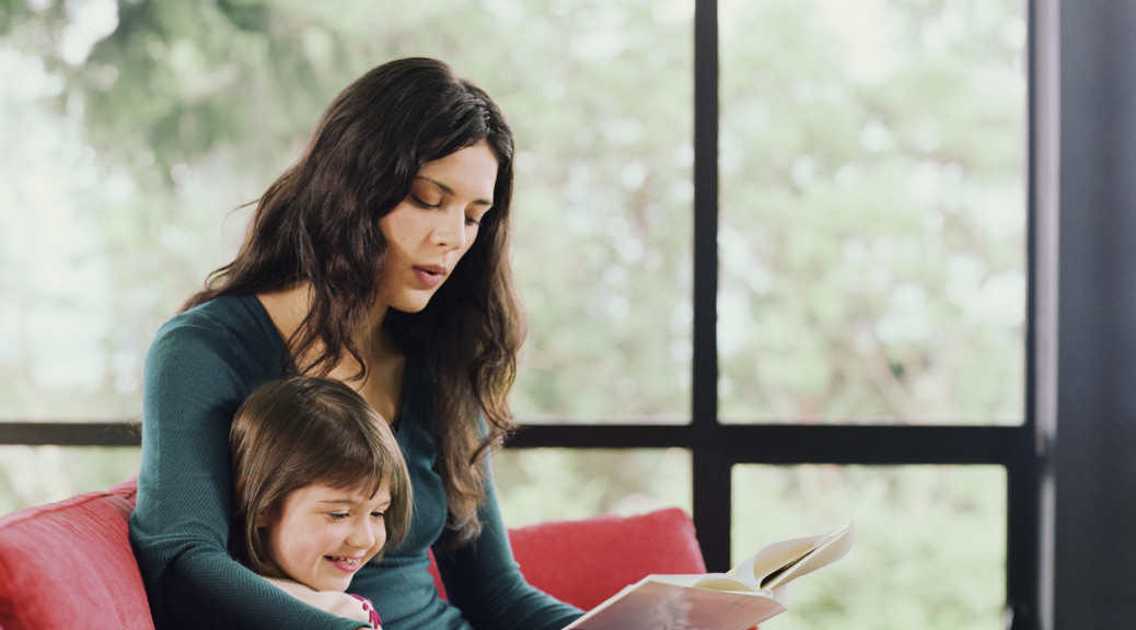 Mother and young daughter sitting on sofa, enjoying reading a book.