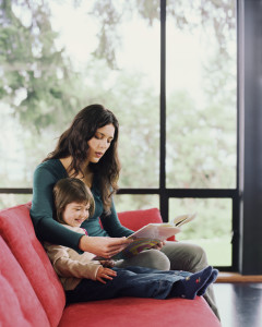 Mother and young daughter sitting on sofa, enjoying reading a book.