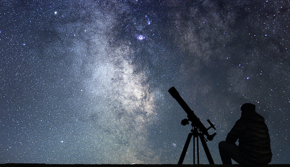 A man gazes up at the stars--his telescope nearby.
