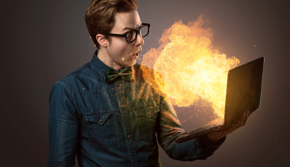 A man holds a laptop that is throwing out a fireball.