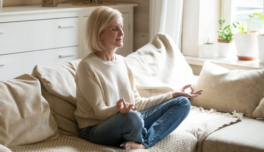 A woman sits on her couch meditating.