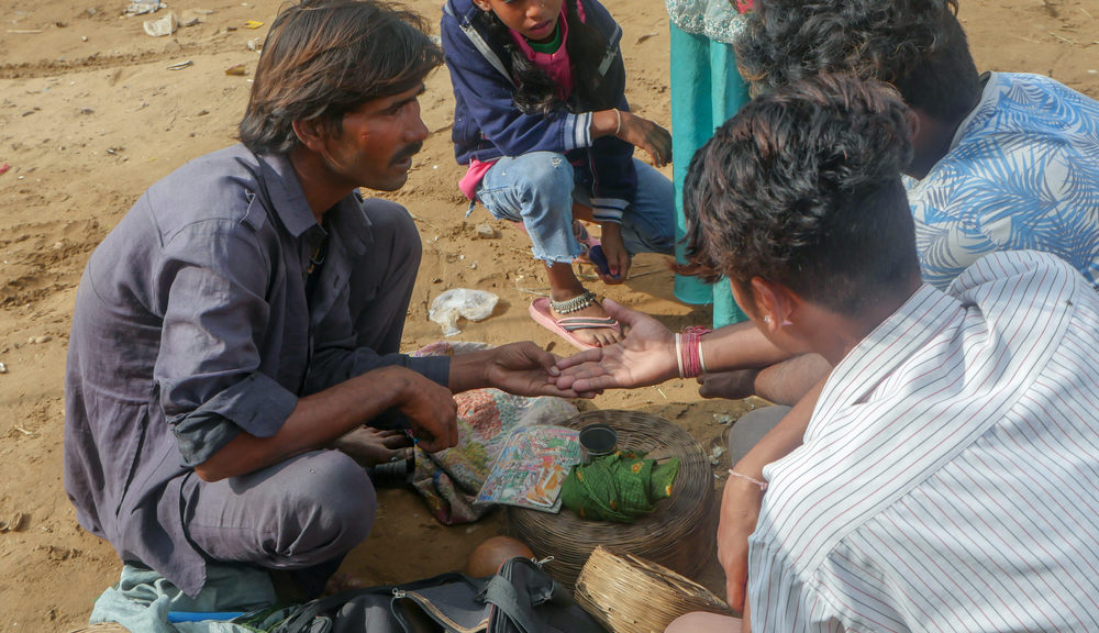 A man squats in the dirt and receives his horoscope from Indian astrology.