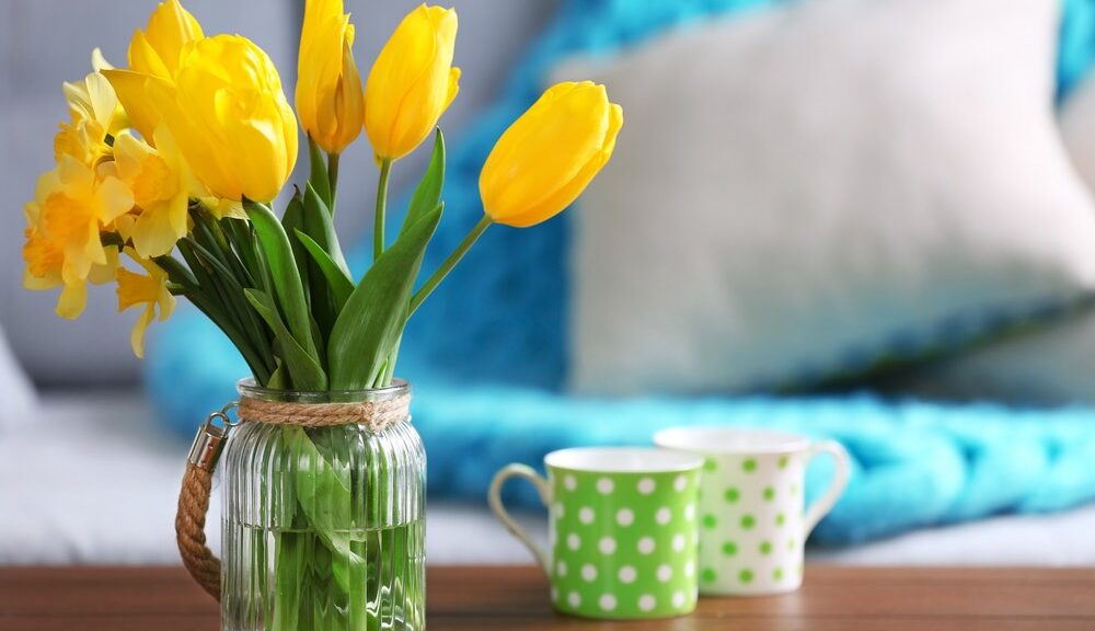 A glass jar of spring flowers sits on a wooden table.