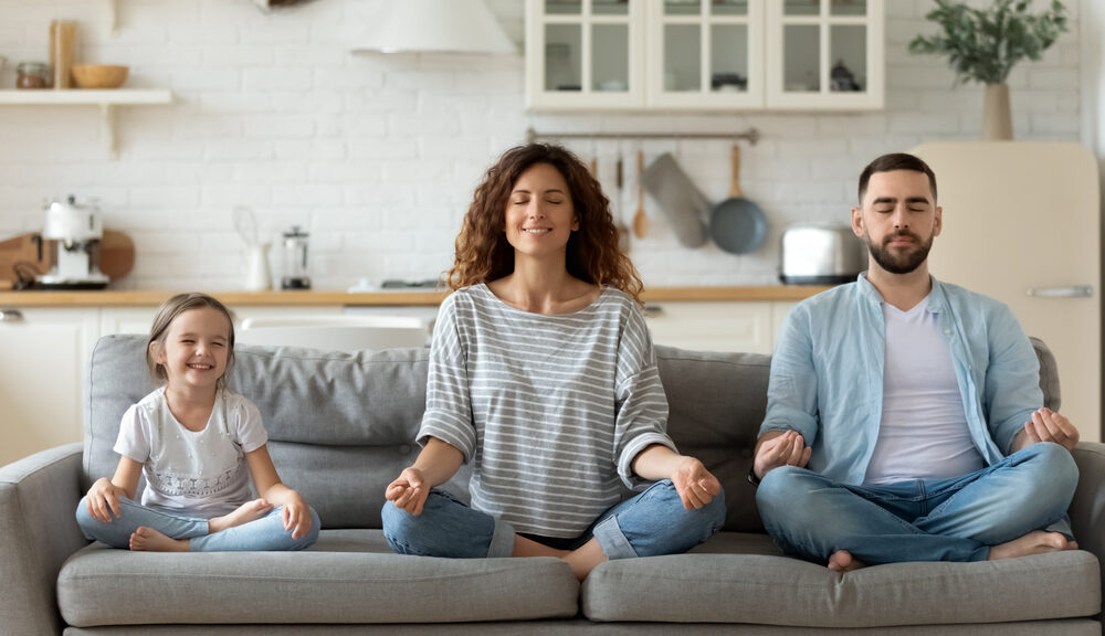 A family sits on the couch meditating.