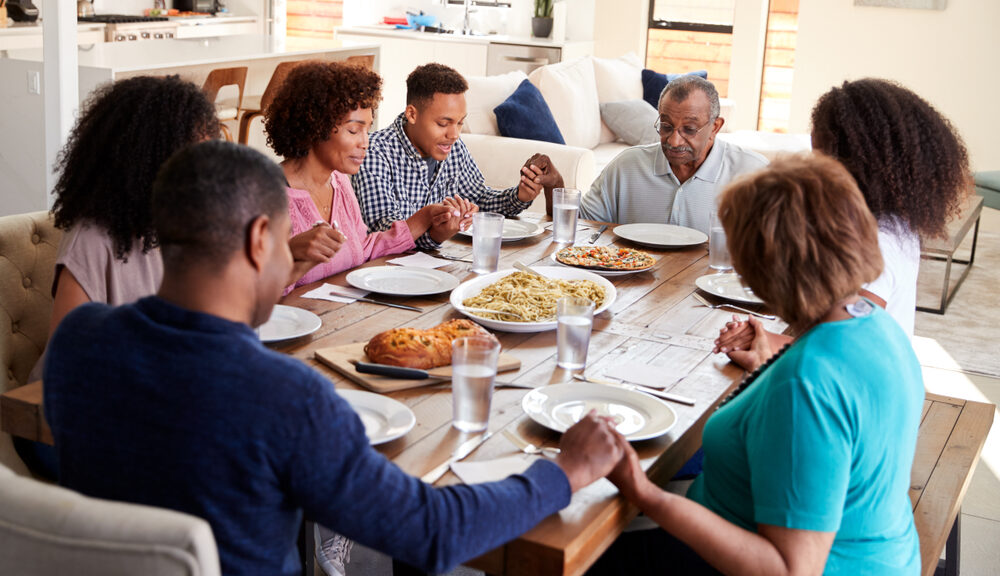 A Black family gathers around a kitchen table for dinner.
