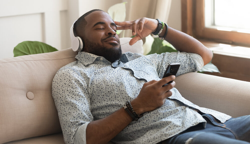 A man relaxes on his couch as he is guided through meditation by one of his meditation apps.