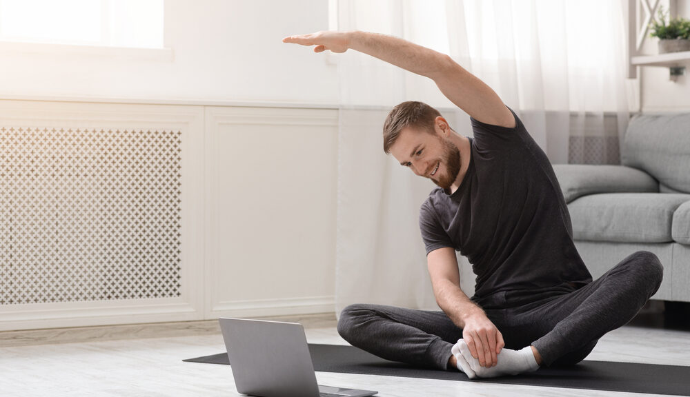 A man in the midst of creating a spiritual self-care routine stretches in front of his computer.