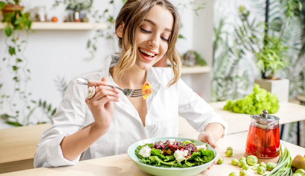 A woman cheerfully eats a salad (I'm not sure how she manages).