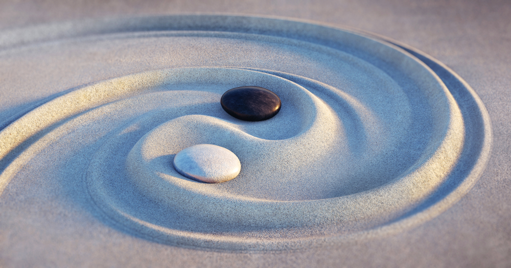 Two stones form the yin and yang symbol in the sand.