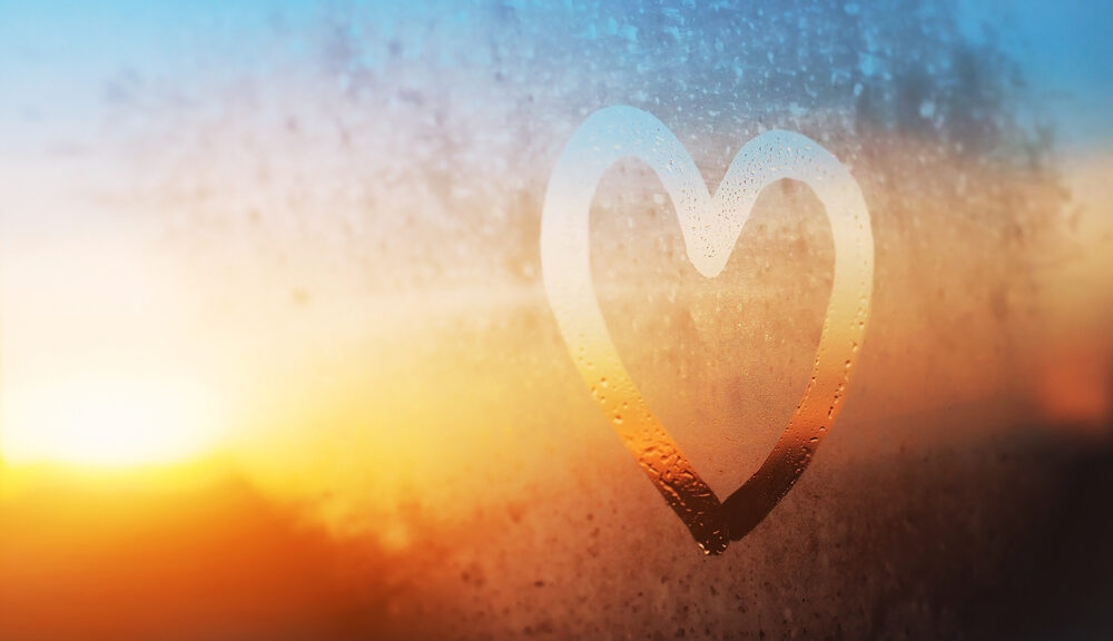spiritual heart drawn in condensation on window looking at sunrise