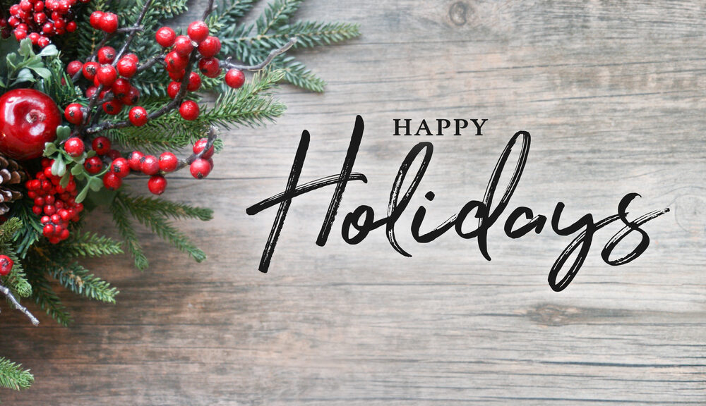 happy holidays on table with greenery and holly berries