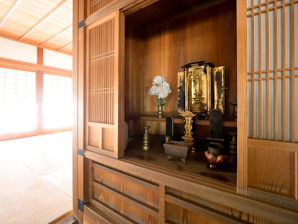A home altar set in a crafted wooden cabinet in a Japanese house with gold idol and white flowers